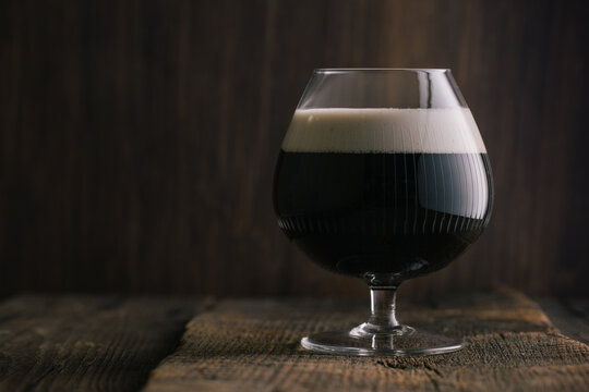 Crystal glass of dark stout beer placed on wooden table in bar
