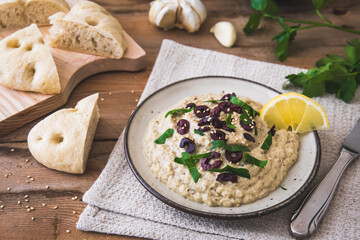 Arabian cuisine: Baba Ganoush with black olives and minced parsley and flatbread on a rustic wooden table