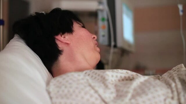 The woman is pushing on the bed in the hospital. It relaxes and strains the body. Holds the handles with your hands. Sweaty face.