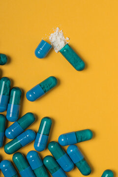 High angle of contents of medical drug poured out of blue colored capsule on yellow background
