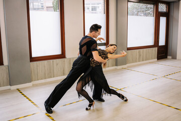 Couple of dancers in elegant wear performing ballroom dance during class in contemporary studio