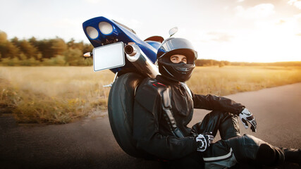 Motorcyclist or biker in a black leather jacket and a protective helmet sits near a stylish sports...