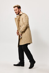 fashionable man in a beige coat and trousers on a light background walks to the side side view