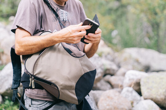Crop anonymous male trekker in sunglasses browsing on smartphone during trip