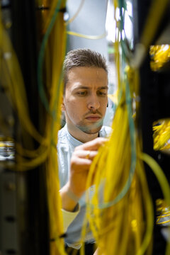 Concentrated male specialists working with wires in server while managing network in data center