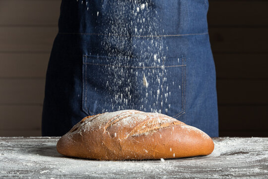 Crop anonymous baker sprinkling flour over fresh bread loaf placed on table while working in bakery