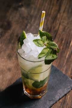 Glass with cold alcohol Mojito cocktail with rum and fresh lime served with ice and mint leaves on wooden table