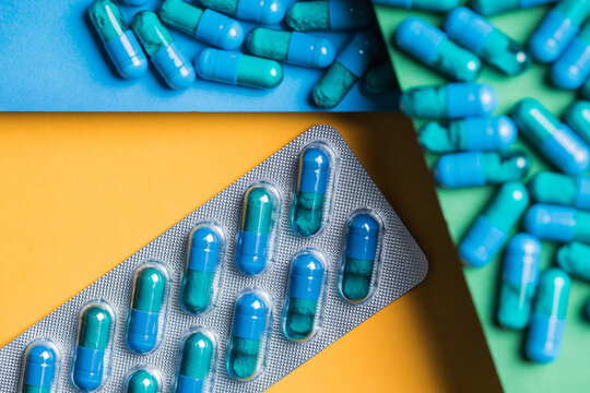 From above of plastic blister packs with blue medical capsules placed on yellow and green and blue background