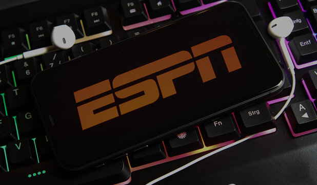 Viersen, Germany - March 1. 2021: Closeup of smartphone screen with logo lettering of online tv and movie streaming service espn on illuminated computer keyboard