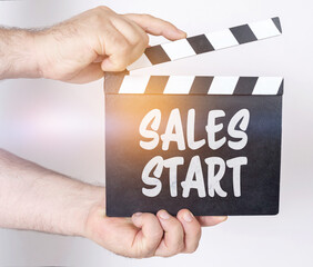 On a white background, a man holds a clapperboard in his hands on which it is written - SALES START