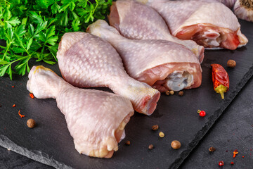Shooting for the catalog. Raw chicken legs with spices and vegetables on a wooden cutting board. Black background. Top view