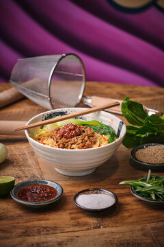 Stock photo of yummy noodles soup with minced meat isolated in wooden background next to sesame seeds and other ingredients.