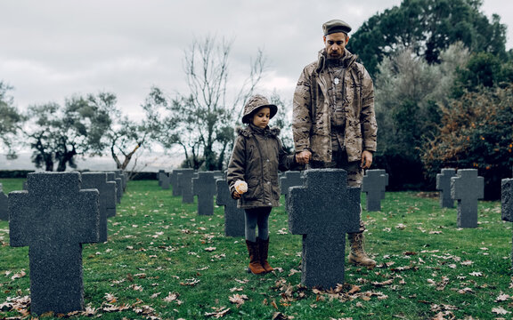 Full body of male warrior holding hands with girl feeling sorrow for deceased hero in cemetery
