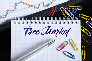 On the desktop are a forex chart, paper clips, a pen and a notebook in which it is written - Free Market