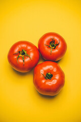 Three ripe red tomatoes on a yellow background. Vegan concept. Fruit. Healthy food.