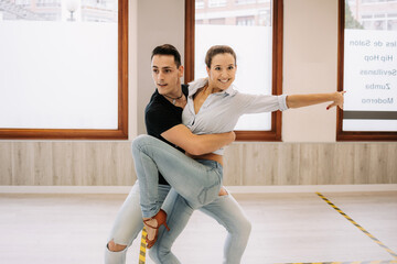 Content skilled couple performing ballroom dance during lesson in bright spacious hall and looking away