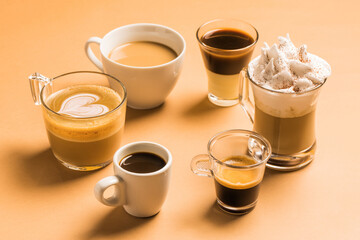 High angle set of different classic kinds of aromatic coffee drinks served in cups of various sizes arranged on beige surface
