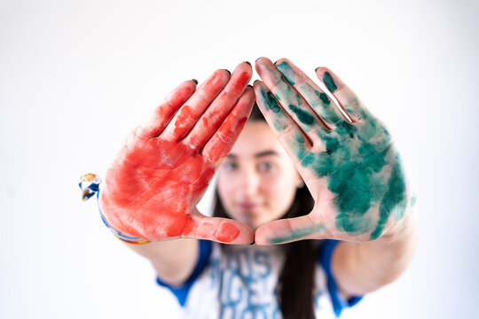 Young female artist looking at camera with stretched arms with red and green paints on palms of hands