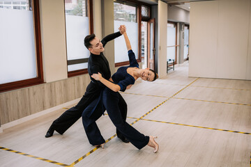 Skilled couple of dancers in elegant clothes rehearsing moves of ballroom dance during class in studio