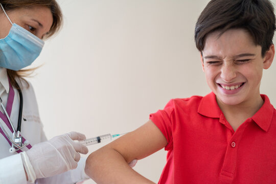 Female medic in mask making injection of vaccine from coronavirus for boy with closed eyes and grimace on face