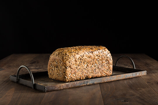 Appetizing crispy freshly baked bread loaf of sourdough bread with crispy crust and grains on metal rusty tray placed on wooden table