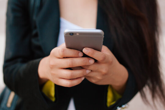 Cropped unrecognizable female entrepreneur in smart casual style standing in street of downtown browsing on mobile phone