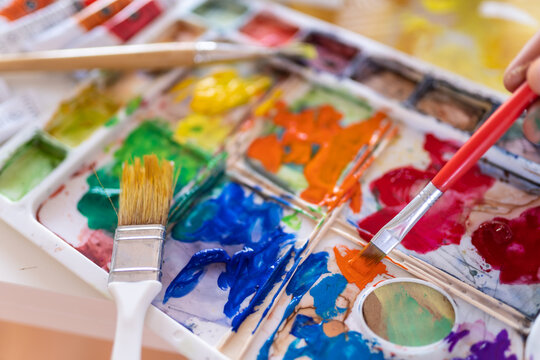 Crop anonymous painter mixing paints with brush using watercolor palette while working in art studio