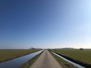 Beautiful day on walking and cycling on an empty and lonely road or cycling path in Wergea Friesland Netherlands. Blue sky. Green fields. Blue water.