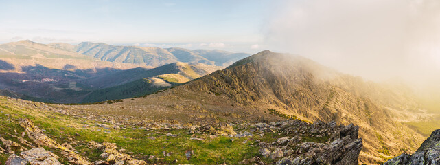 Picturesque panoramic view of high ridges under glowing blue sky with clouds in sunlight
