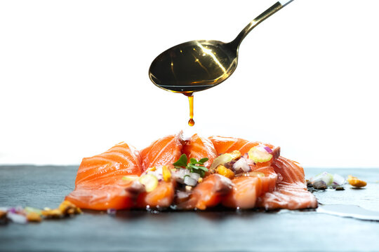 Unrecognizable person adding spoon of soy sauce on delicious salmon fillet dish garnished with herbs against white background