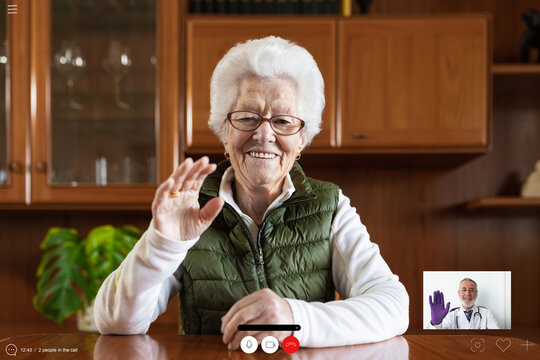 Friendly elderly female showing greeting gesture against tablet while video chatting in house