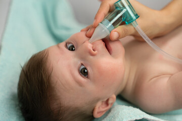 Crop caring mother placing suction machine into adorable baby nostril to remove mucus