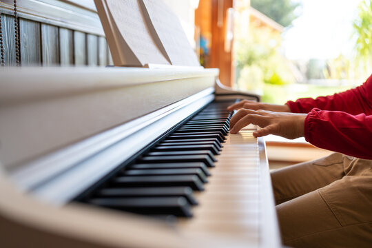 Cropped anonymous child playing piano while reading notes and rehearsing song at home