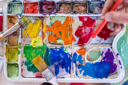 Crop anonymous painter mixing paints with brush using watercolor palette while working in art studio