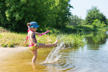 Happy little girl swimming and splashing in the lake on a hot sunny day