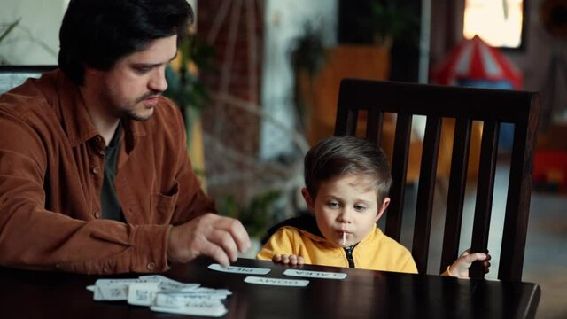 Father teaches a little boy a words from cards under the ABA therapy program at home at the table