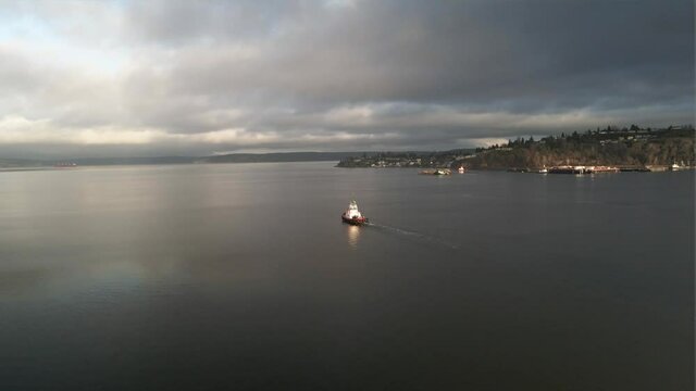 A lone tugboat makes its way across calm open water, storm clouds on the horizon, aerial orbit