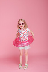 girl in sunglasses and an inflatable water circle on a pink background