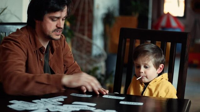 Father teaches a little boy a words from cards under the ABA therapy program at home at the table