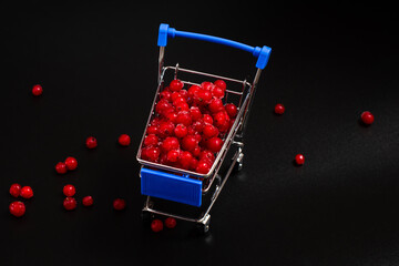 Frozen red currant berries in a small shopping cart on a black background.