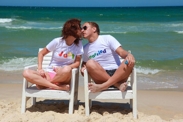 Beautiful girl and guy on vacation sitting on chairs and kissing on the background of the sea. Just...