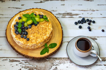 Homemade Napoleon cake (Mille-feuille) decorated with grapes, blueberries and mint leaves on a wooden table.