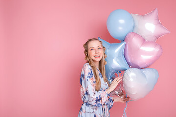 Positive emotional woman with a bunch of balloons on a pink background