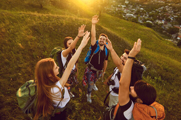 High angle of team of happy tourists reaching out for high five while hiking on grassy hill