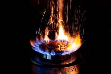 Closeup shot of blue fire from domestic kitchen stove top. Gas cooker with burning flames of propane gas. Red sparks.