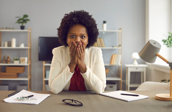 Shock and surprise emotion. Portrait of overwhelmed shocked young african american woman covering mouth with hands after getting promotion at work sitting at office desk. Secret sharing and gossiping