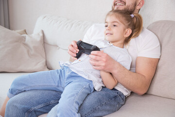  Dad is playing video games on sofa with daughter. Happy family, activity at home, life at home.