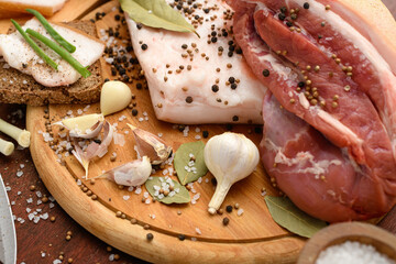 raw pork meat and lard with salt, spices and garlic on a cutting board, dark wooden background