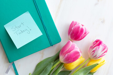bouquet of tulips and journal with note start today on a wooden background
