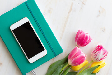 cell phone, journal notebook and tulip flowers on white wood background with copy space